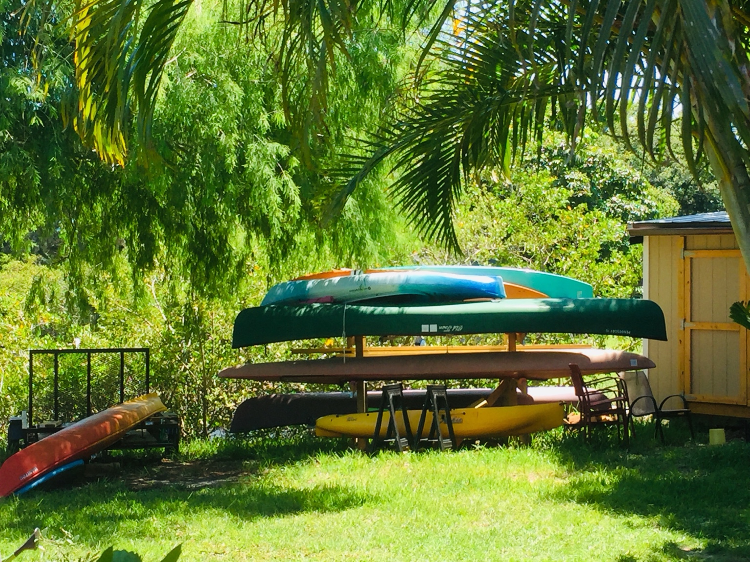 Years of canoes, kayaks, and paddleboards stacked beneath the palms and ready for adventure.