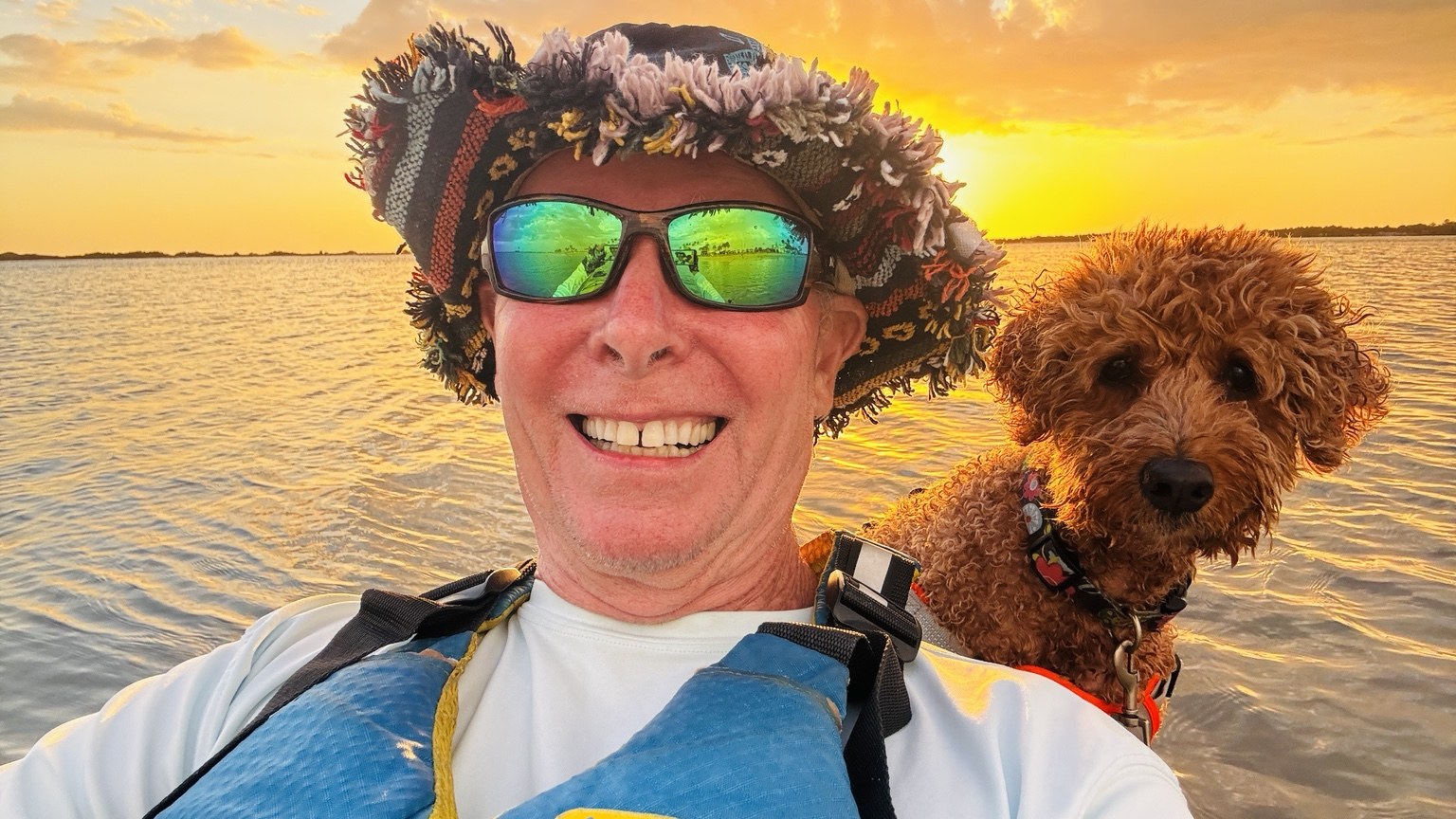 Golden-hour paddle selfie with Buddyboy riding along like the tiny curly-haired admiral of the Gulf.