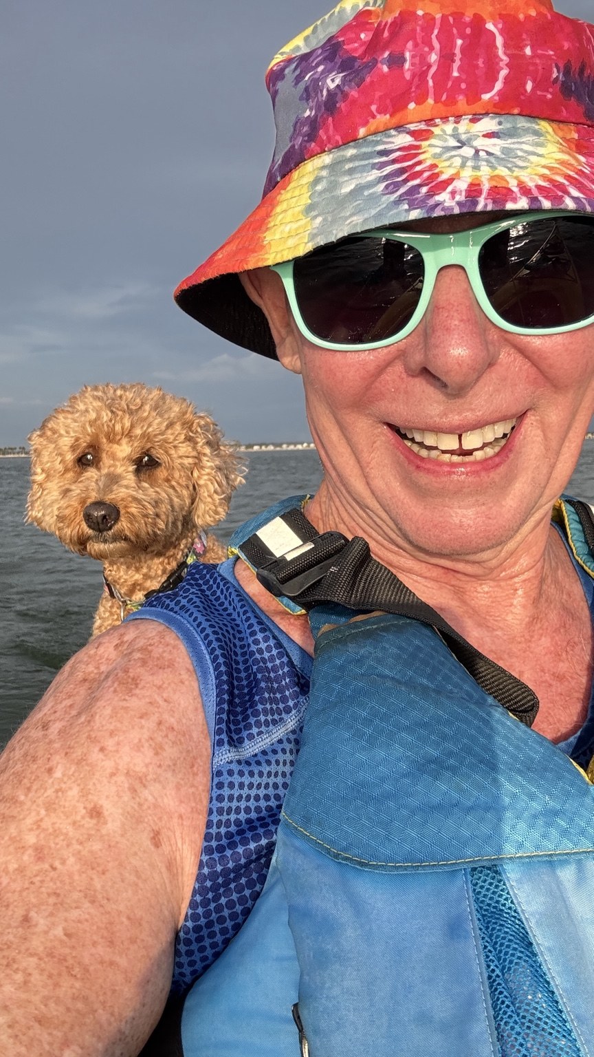 Tie-dye, sunshine, life jacket, and a furry co-captain keeping watch from behind.
