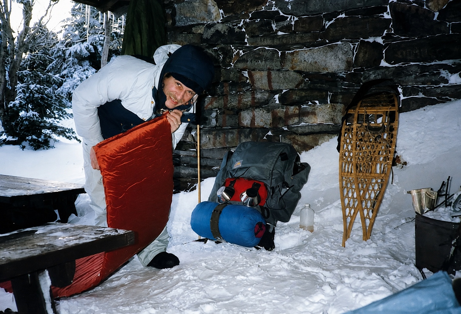 Dan blowing up the Therm-a-Rest in the snow-covered stone shelter, with borrowed wooden snowshoes nearby