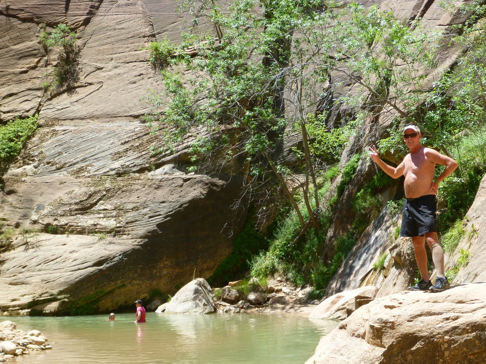 A quiet pool tucked beneath smooth sandstone and green canyon vegetation.