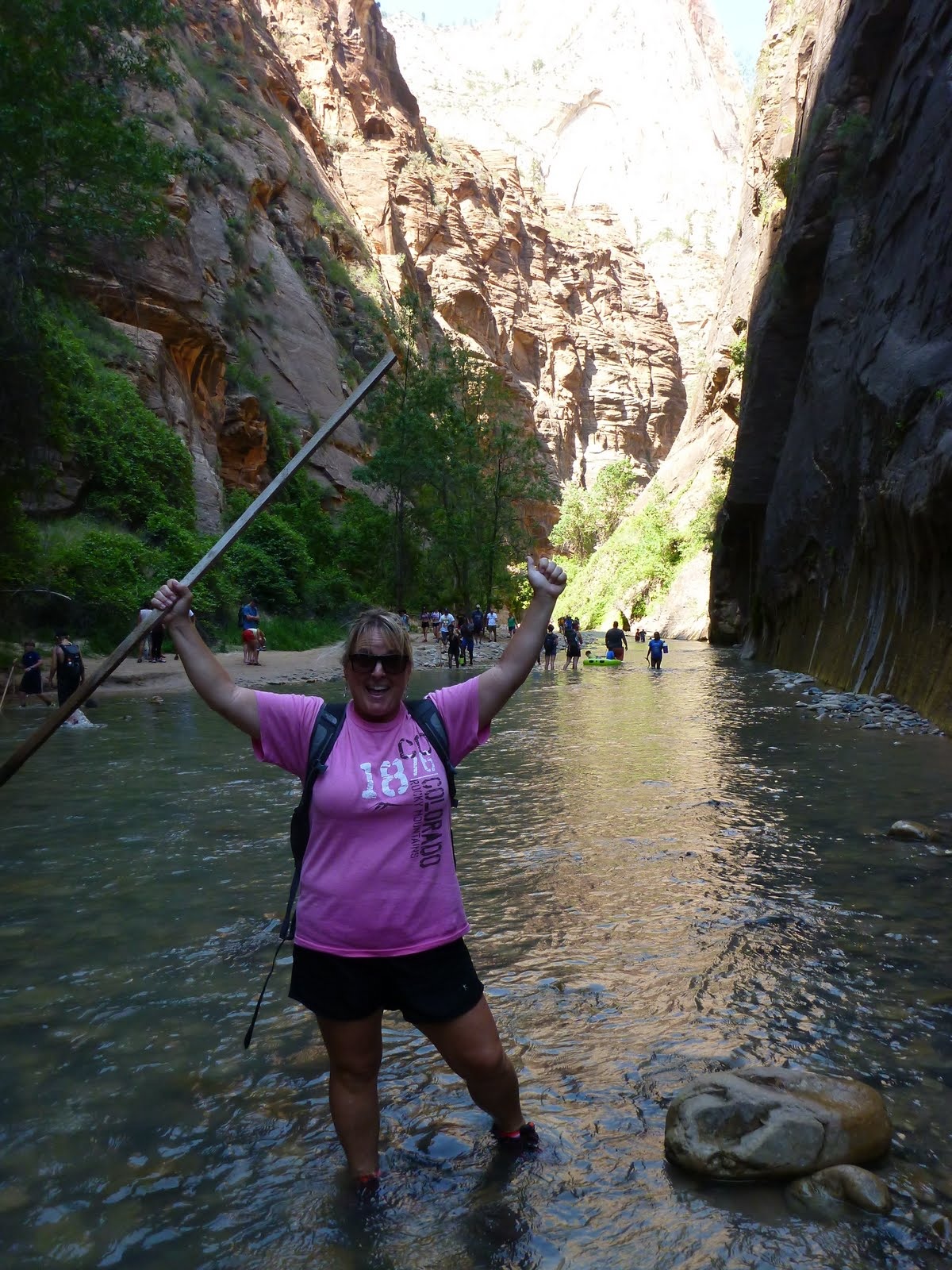 Cindy raising her walking stick in a shaded section of the river.