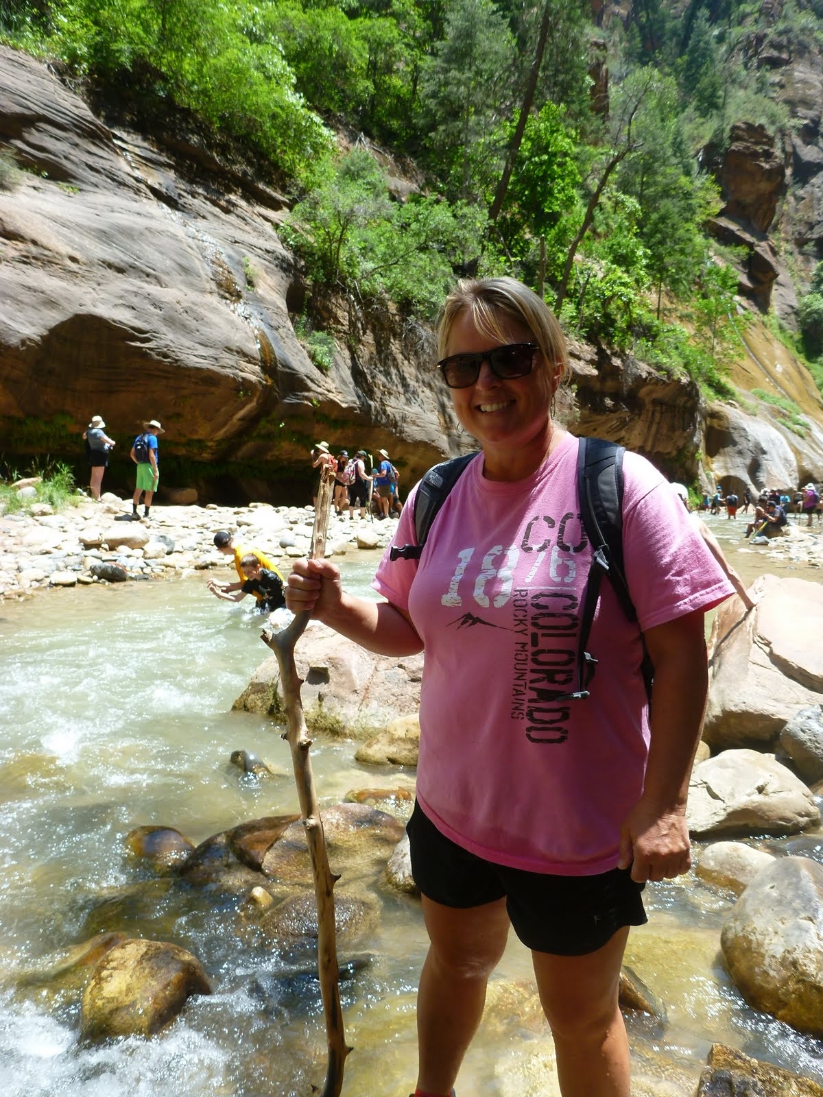 Cindy using a sturdy walking stick to balance on the river stones.