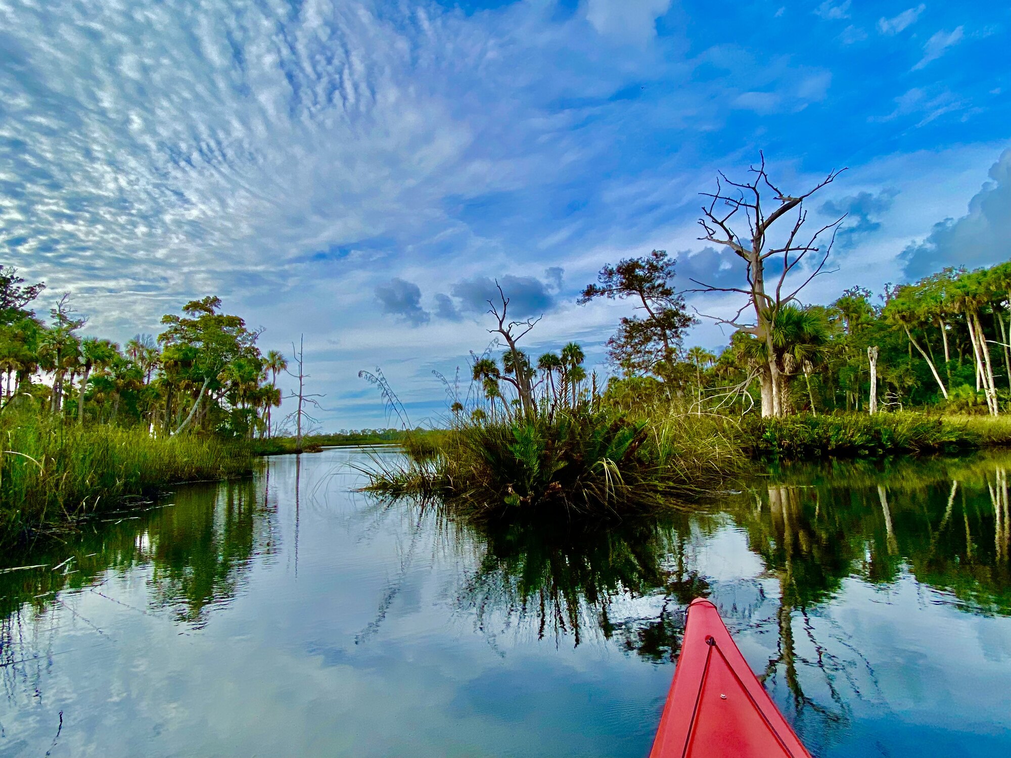 Red kayak entering a narrow marsh waterway