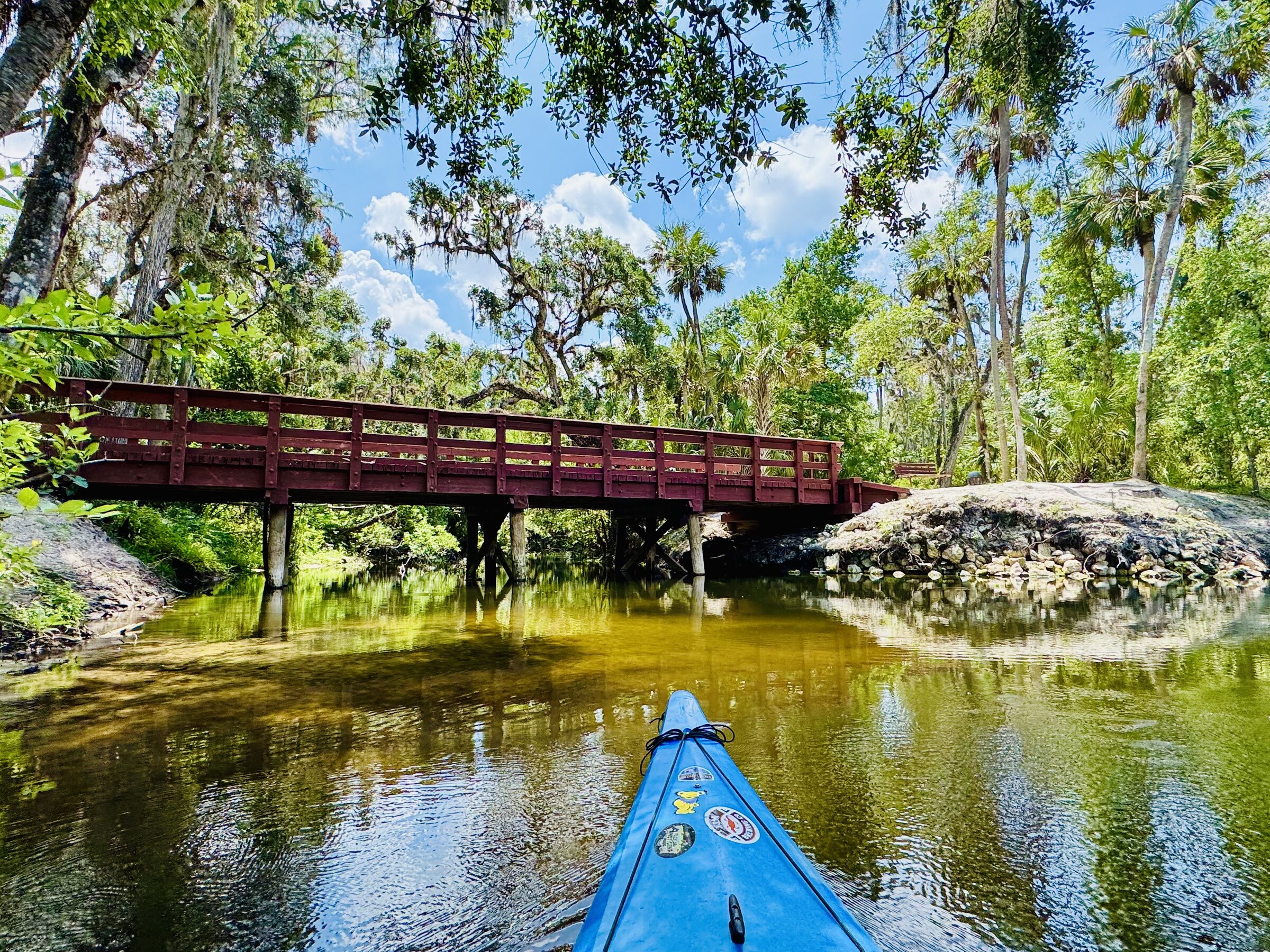A red bridge crossing the river ahead of a blue kayak