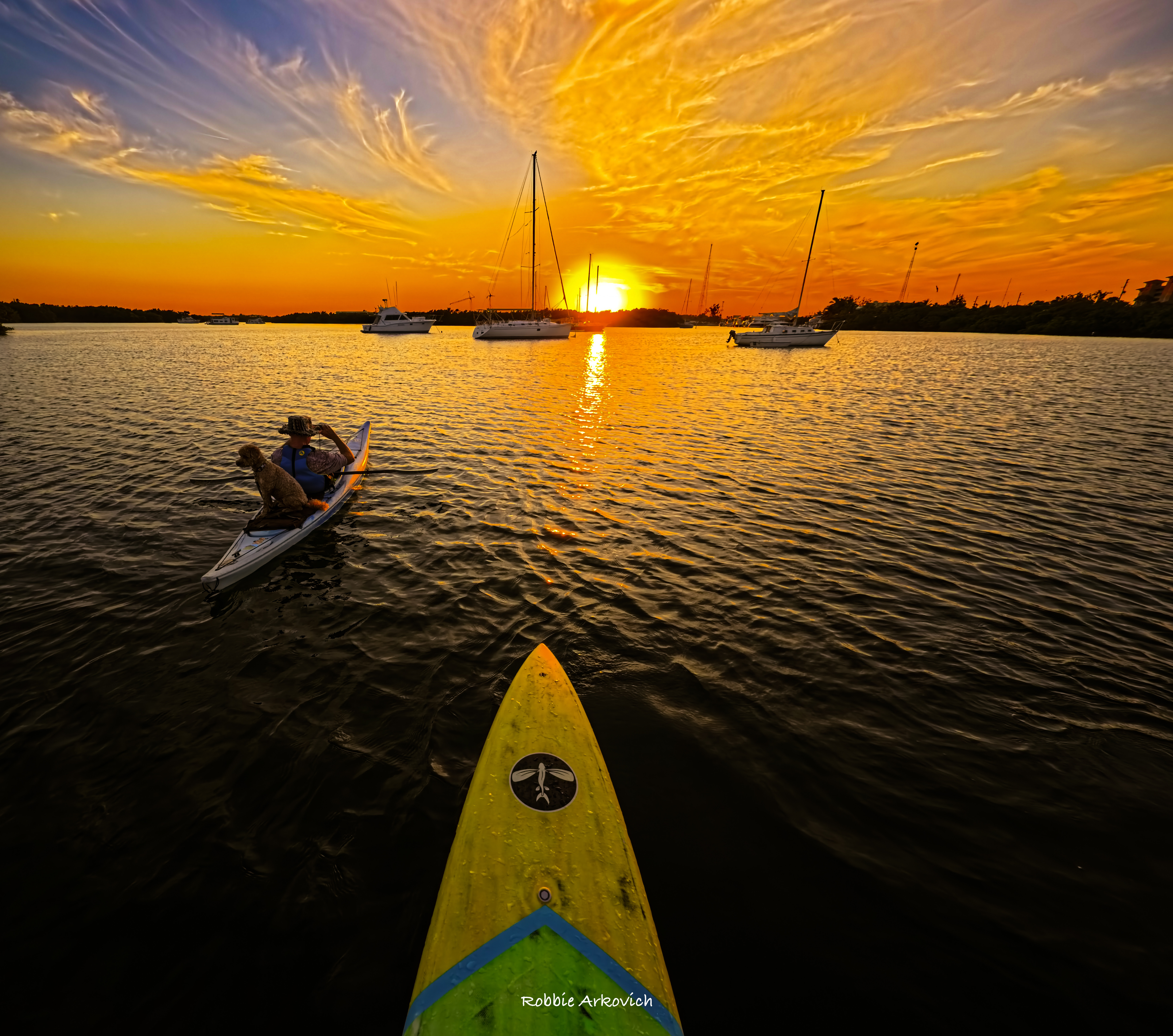 Robbie paddling between sailboats during a brilliant Gandy sunset