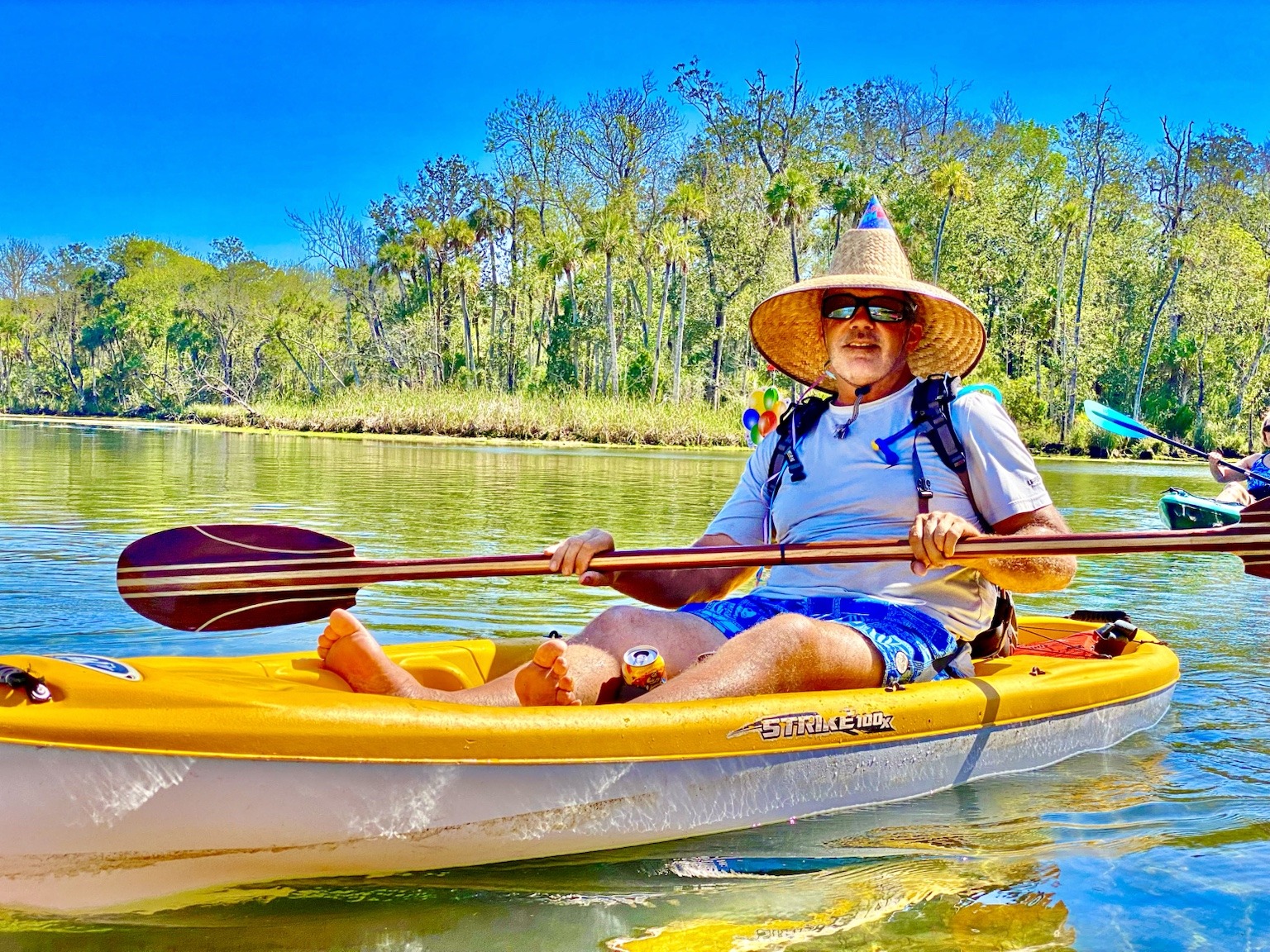 Layne paddling a yellow kayak—the birthday hat turning an ordinary Chaz scene into a birthday parade.