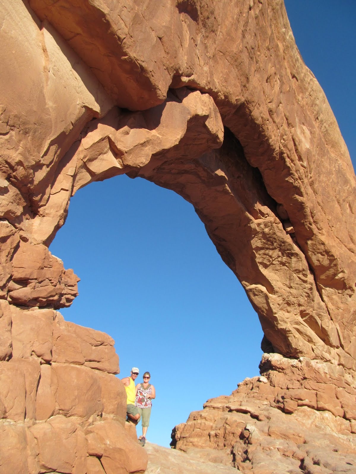 Cindy beneath the towering curve of a natural arch.