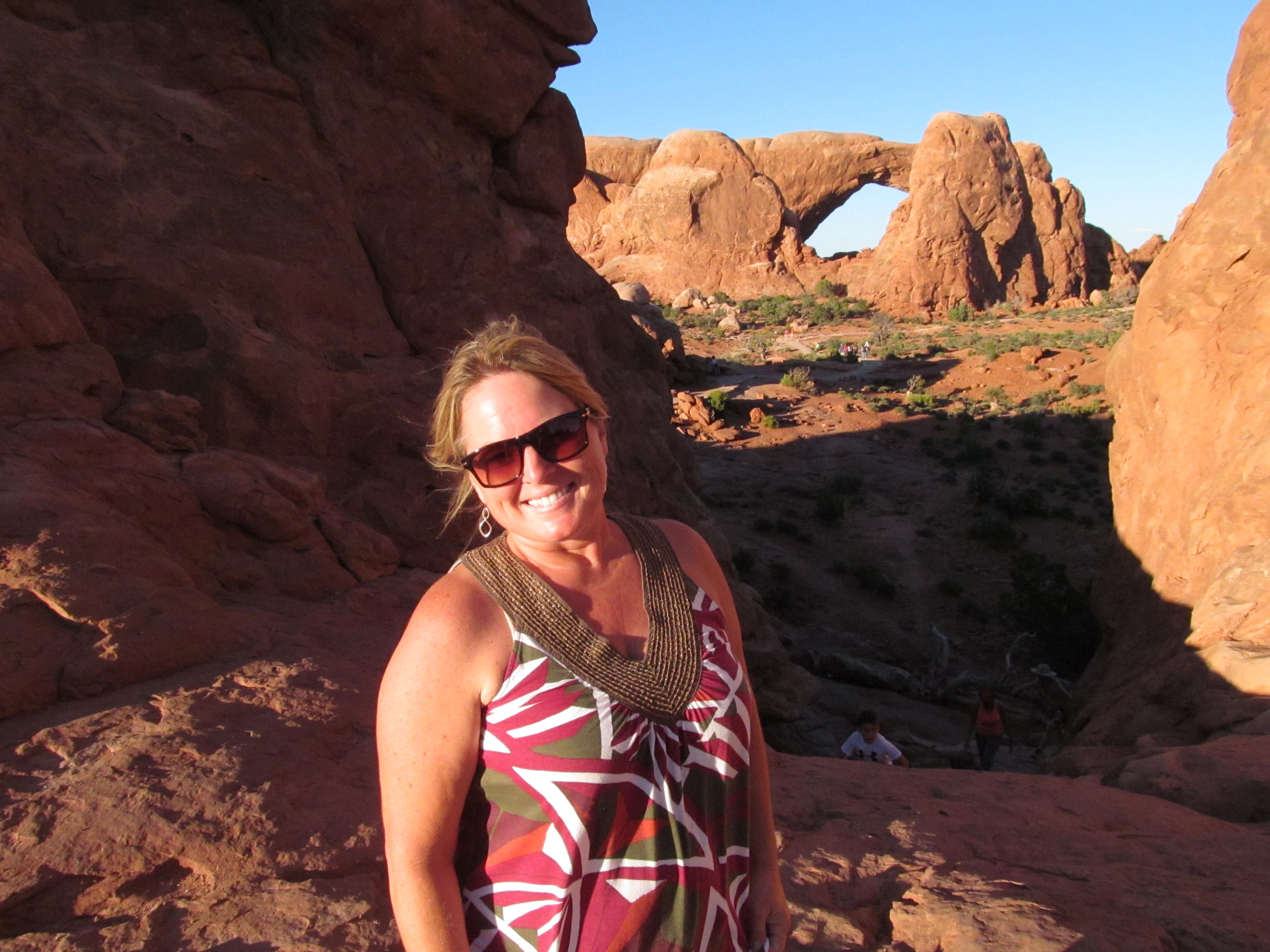 Cindy with natural arches and red rock formations behind her.