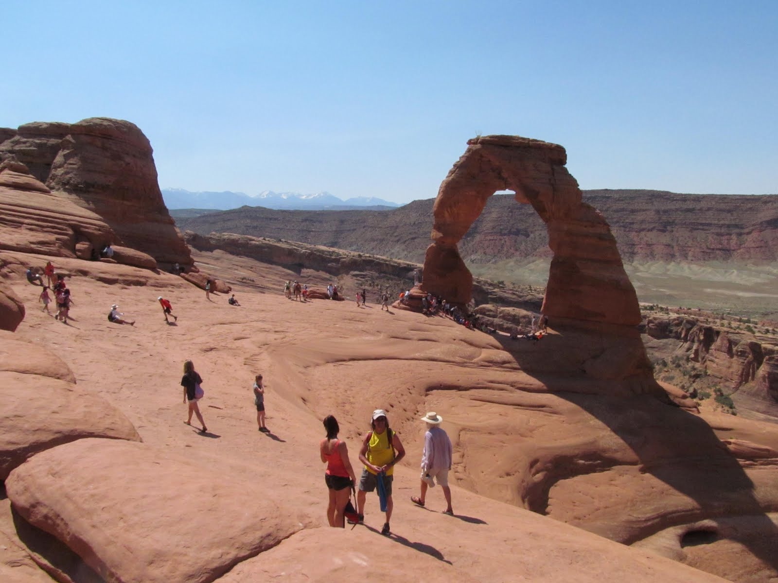 Delicate Arch with hikers gathered around its immense sandstone opening.