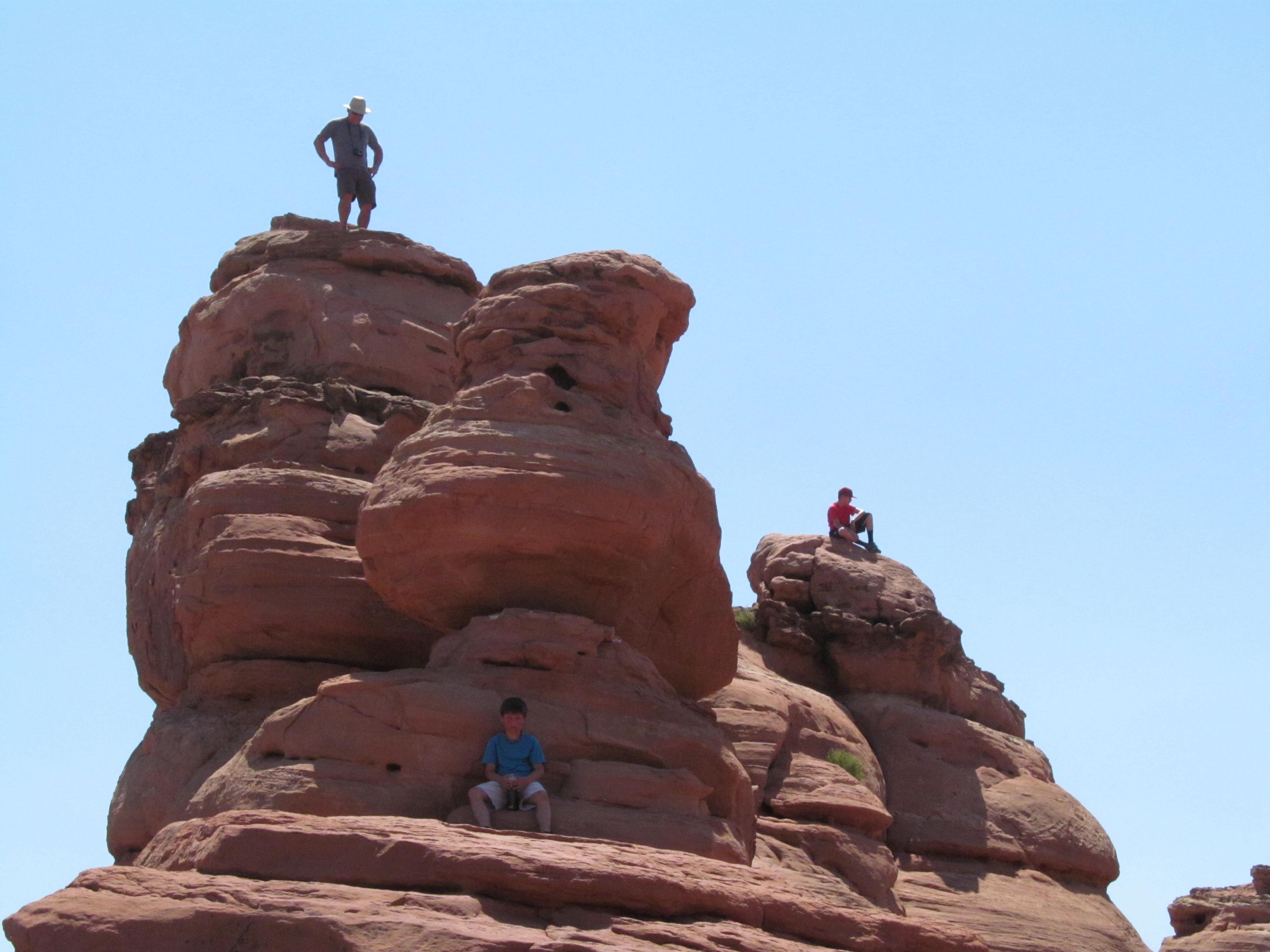 A hiker standing high on a sandstone pinnacle near Delicate Arch.