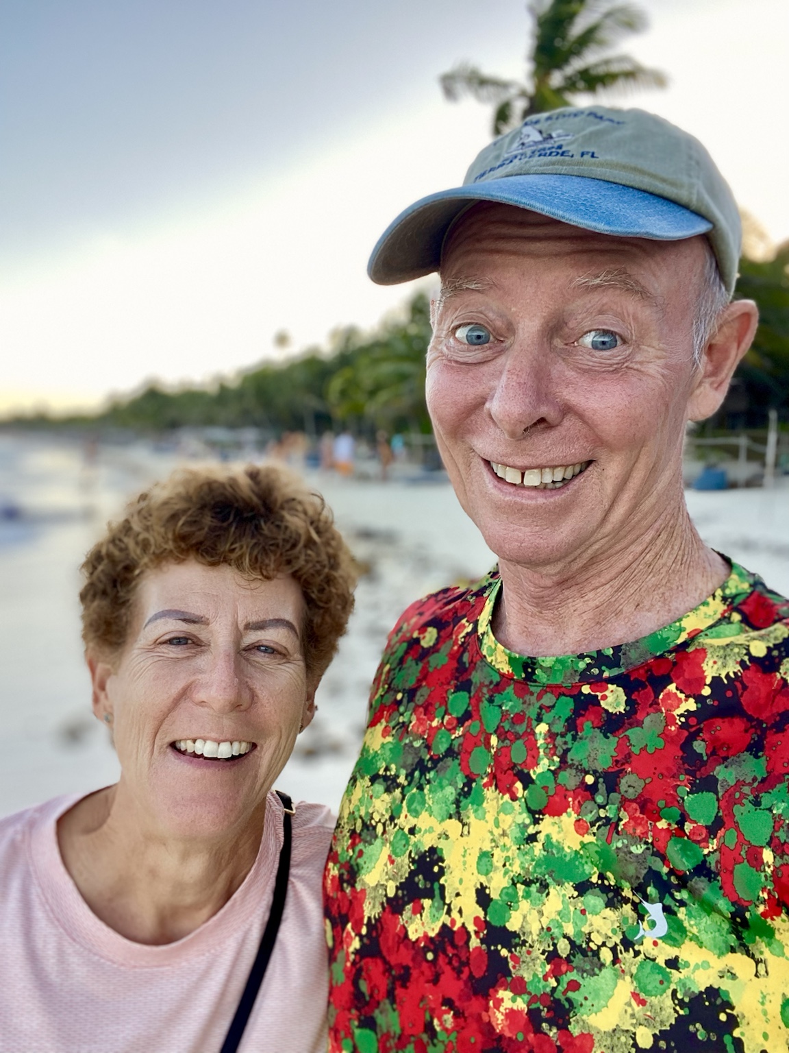 A close beach selfie with palms and the shoreline softly blurred behind them.