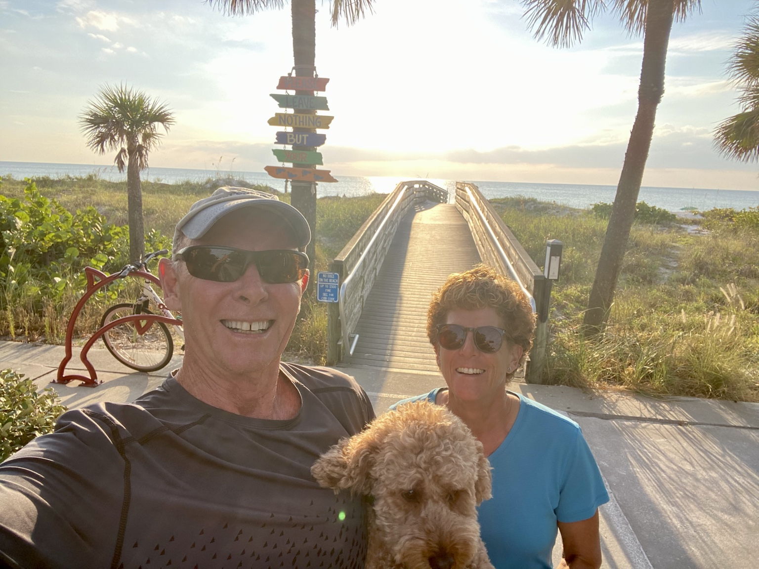 Tim, Kym, and Buddyboy at the beach entrance with the sun shining over the Gulf.
