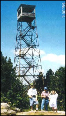 People standing below an old fire tower on a Midstate Trail hike