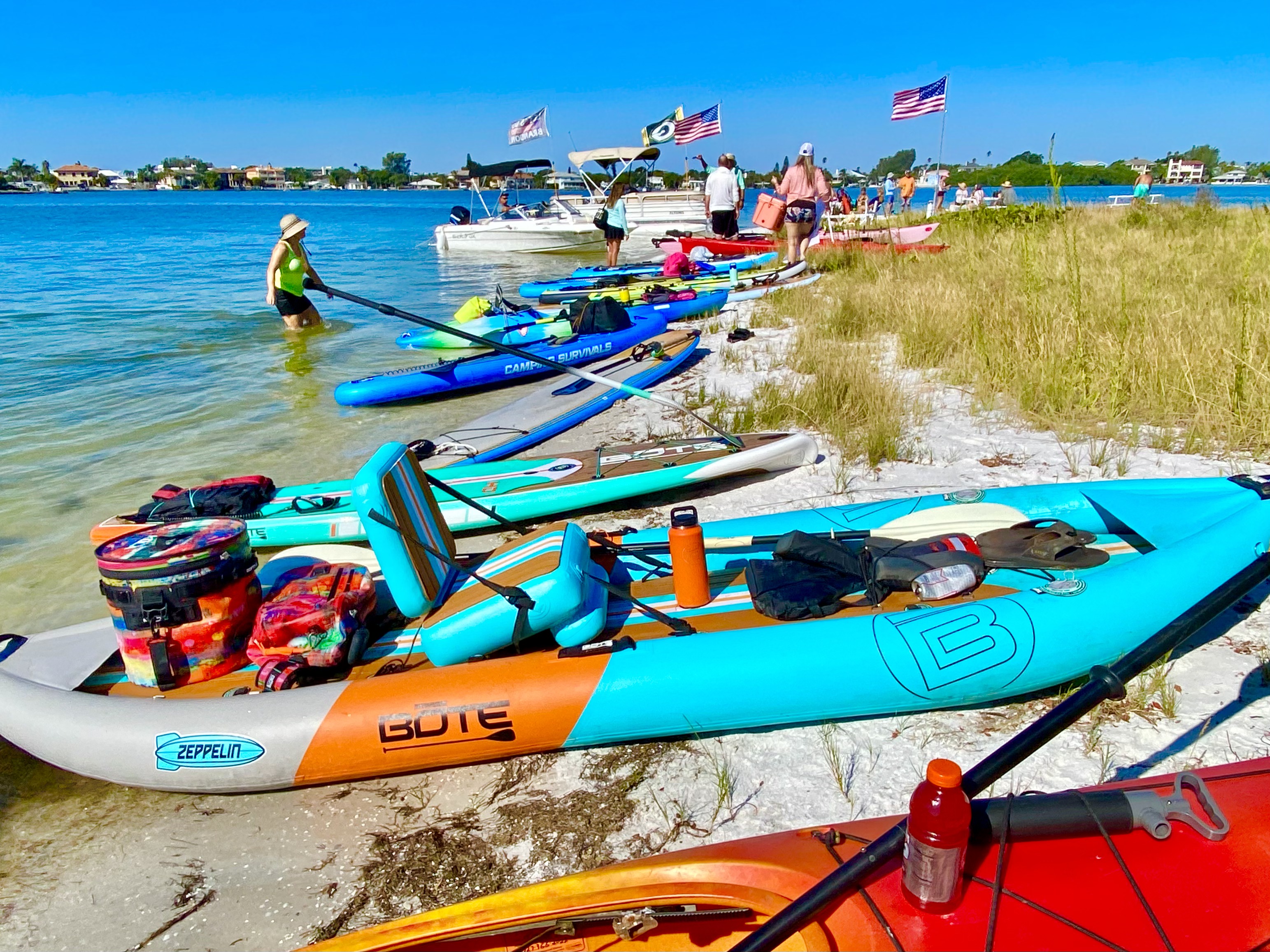 A bright lineup of kayaks and paddleboards rests along the sandy island edge.