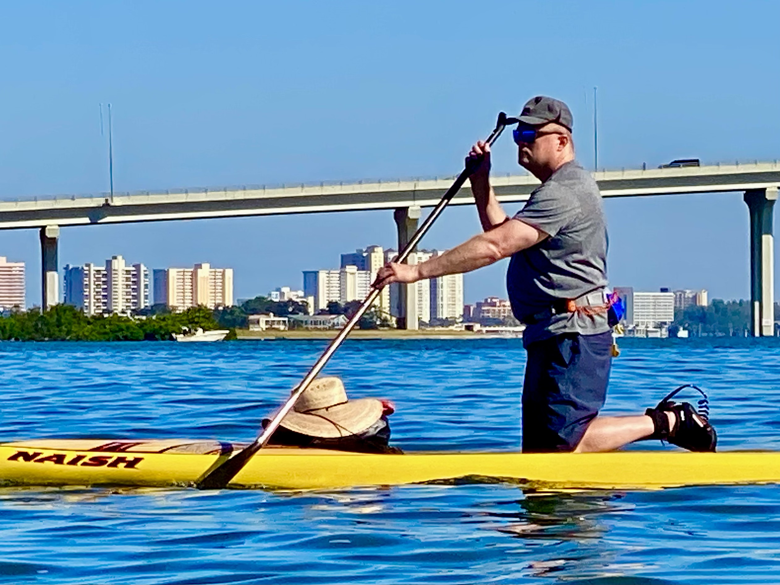 A stand-up paddler moves beneath the broad span of the Belleair Causeway bridge.