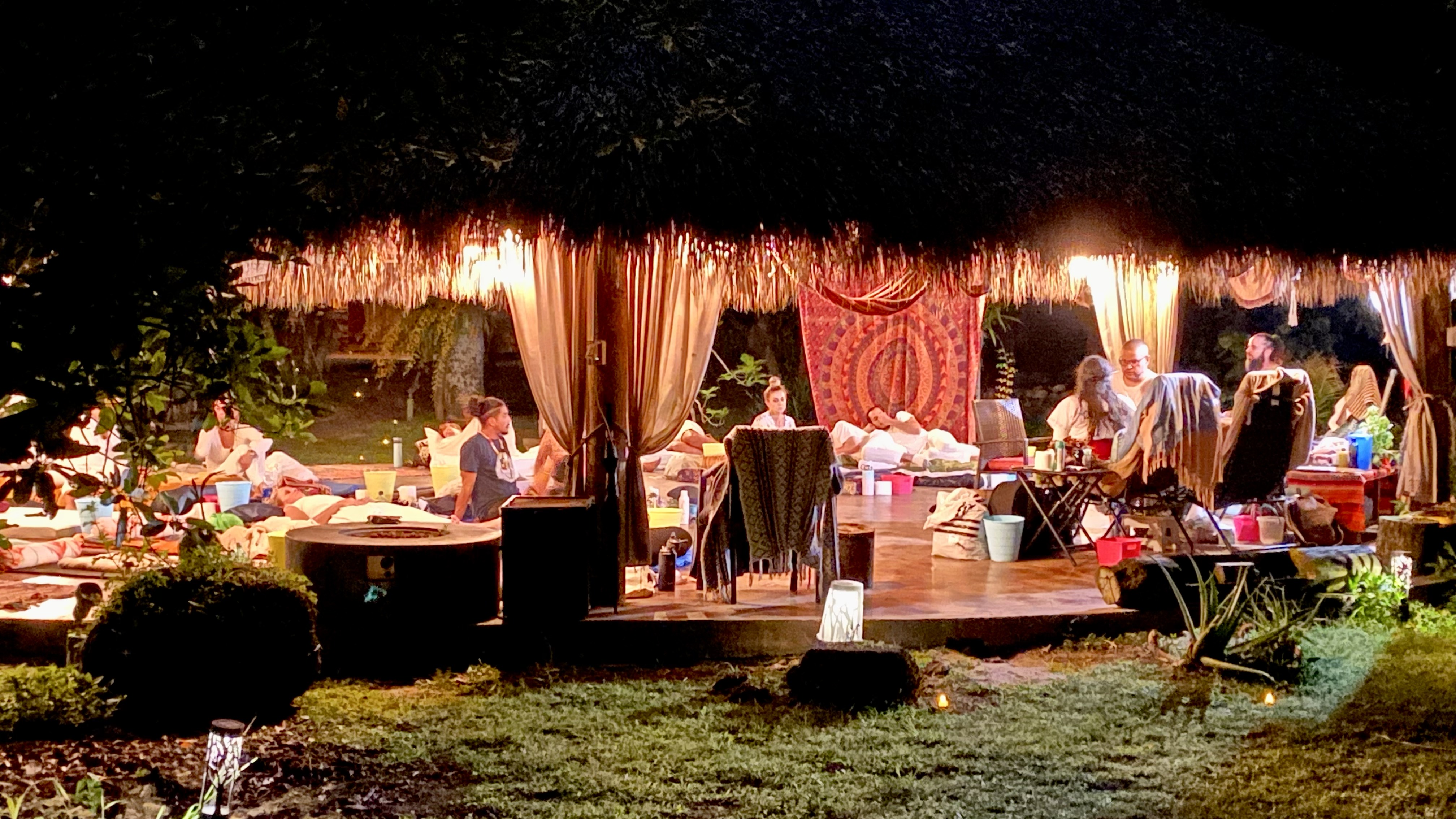 A wide view of the group gathered beneath the thatched pavilion.