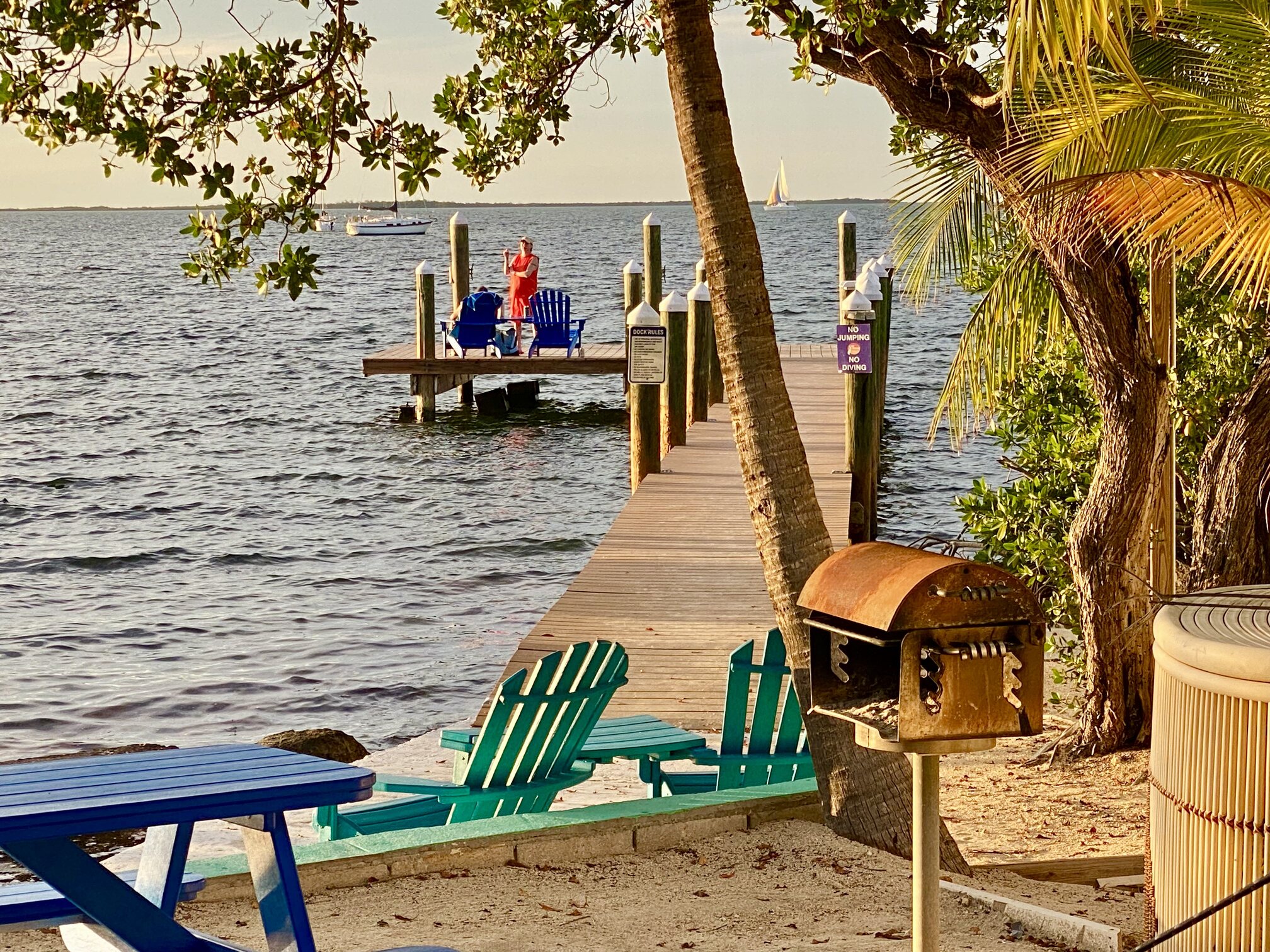 Adirondack chairs beside the water at sunset.