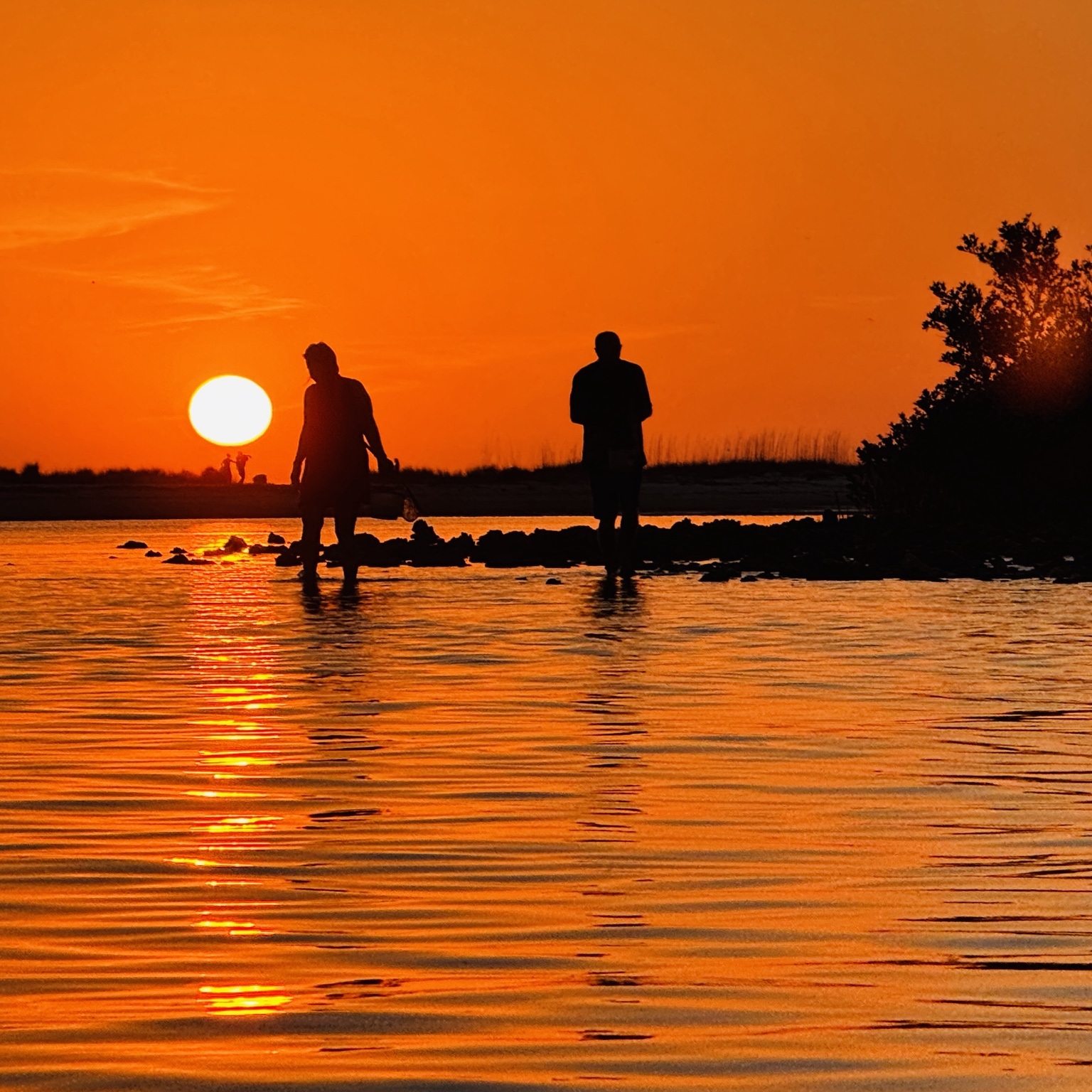 Silhouetted people wading beneath an orange sunset at Hurricane Pass