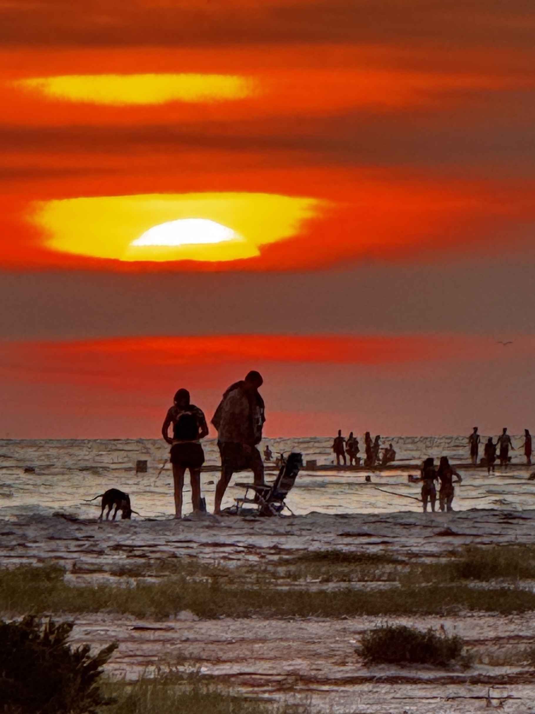 A red sun silhouetting people on the tidal flats