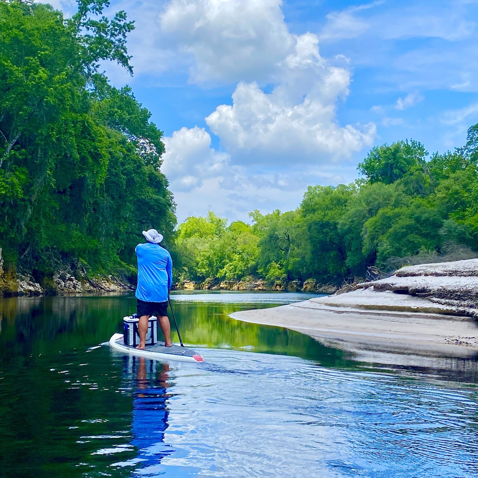 A stand-up paddler crossing a broad, calm reach beneath a bright blue sky.
